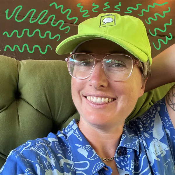 A person wearing the green Crucial Comix hat grins at the camera.