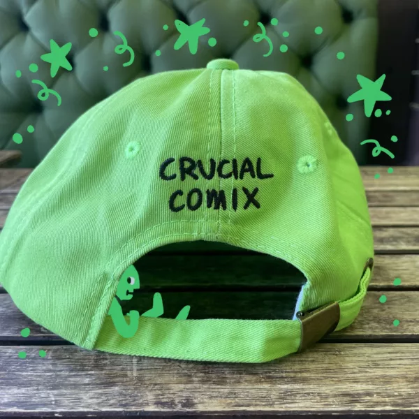 The back of the Crucial Comix hat has the text "crucial comix" embroidered in black, and an adjustable strap fastened with a bronze colored fastener.